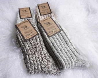 May include: Two pairs of wool socks with ribbed texture, in shades of gray and brown, are displayed on a white, fluffy surface. Each pair has a brown tag with the text "Naturwarm Wolle" and size 39-42.