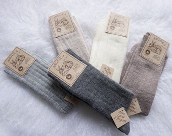 May include: Four pairs of socks in different colours: grey, beige, white, and dark grey. Each pair has a brown tag with the text "Angora" and a picture of a rabbit. The dark grey socks have a tag with the text "Avec Laine d'Angora".