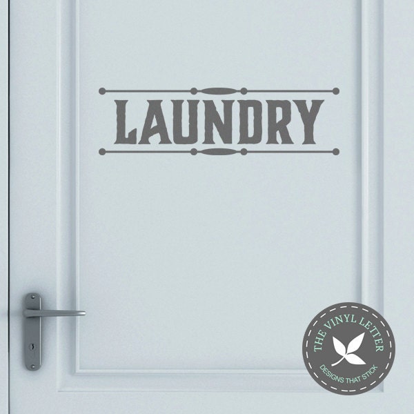 May include: A white door with a gray vinyl decal that says "LAUNDRY" in a vintage style font. The decal is framed by two horizontal lines and a decorative design. A small gray circle with white text says "The Vinyl Letter Designs That Stick" in the bottom right corner.