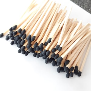 May include: A bunch of wooden matches with black tips. The matches are arranged in a pile, with the tips facing up.