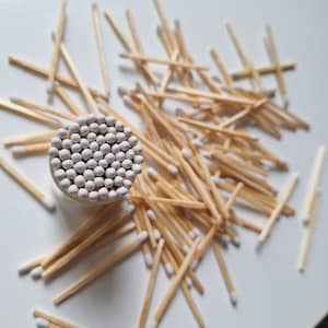 Può includere: Primo piano di un barattolo di vetro pieno di teste di fiammiferi bianche. Il barattolo è circondato da un mucchio di fiammiferi di legno con punte bianche.