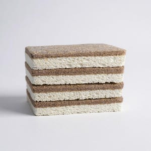 May include: A stack of rectangular cleaning sponges. Each sponge has a light brown, textured top and bottom layer, with a white, porous middle layer. The sponges are stacked neatly on a white surface.