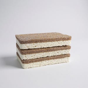 May include: A stack of four rectangular cleaning sponges. Each sponge has a light brown top and bottom layer with a cream-colored middle layer. The sponges are stacked neatly on top of each other against a white background.