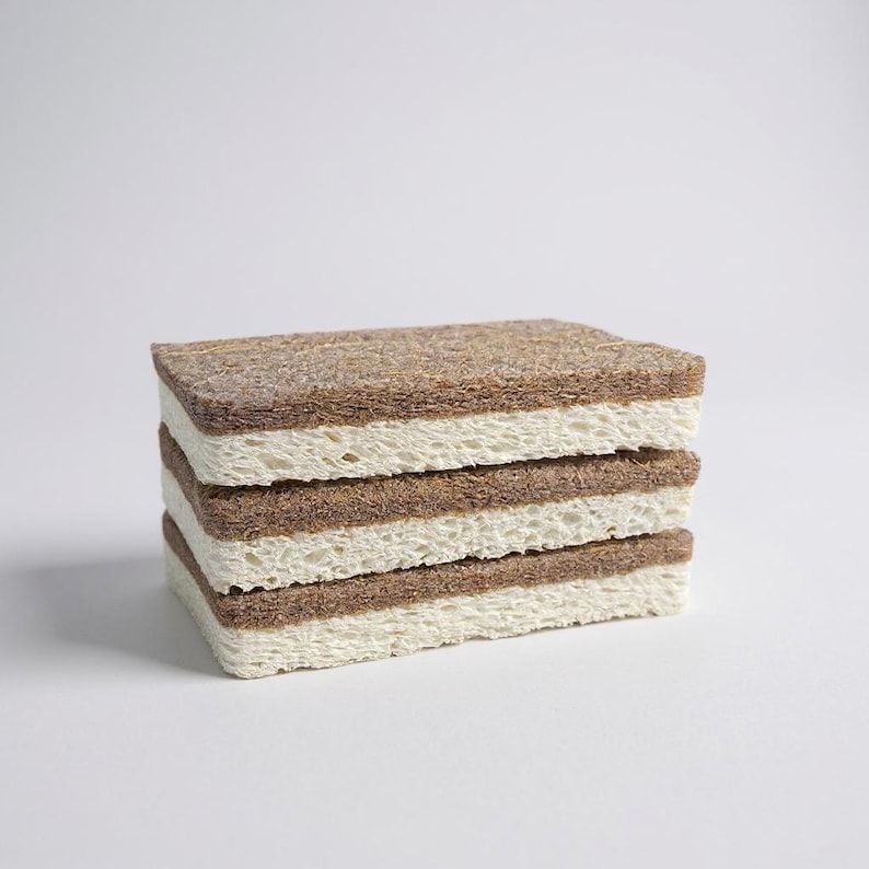 May include: A stack of four rectangular cleaning sponges. Each sponge has a light brown top and bottom layer with a cream-colored middle layer. The sponges are stacked neatly on top of each other against a white background.