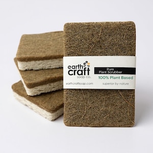 May include: A stack of four rectangular, plant-based scrubbers. The scrubbers are brown with a white layer on one side. The front scrubber has a white band with the text "earth craft soap co." and "Pure Plant Scrubber 100% Plant Based".