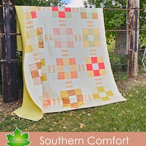 May include: A quilt with a patchwork design in shades of yellow, orange, and red. The quilt is hanging on a fence with a green grassy background. The text "Southern Comfort" is printed below the quilt.