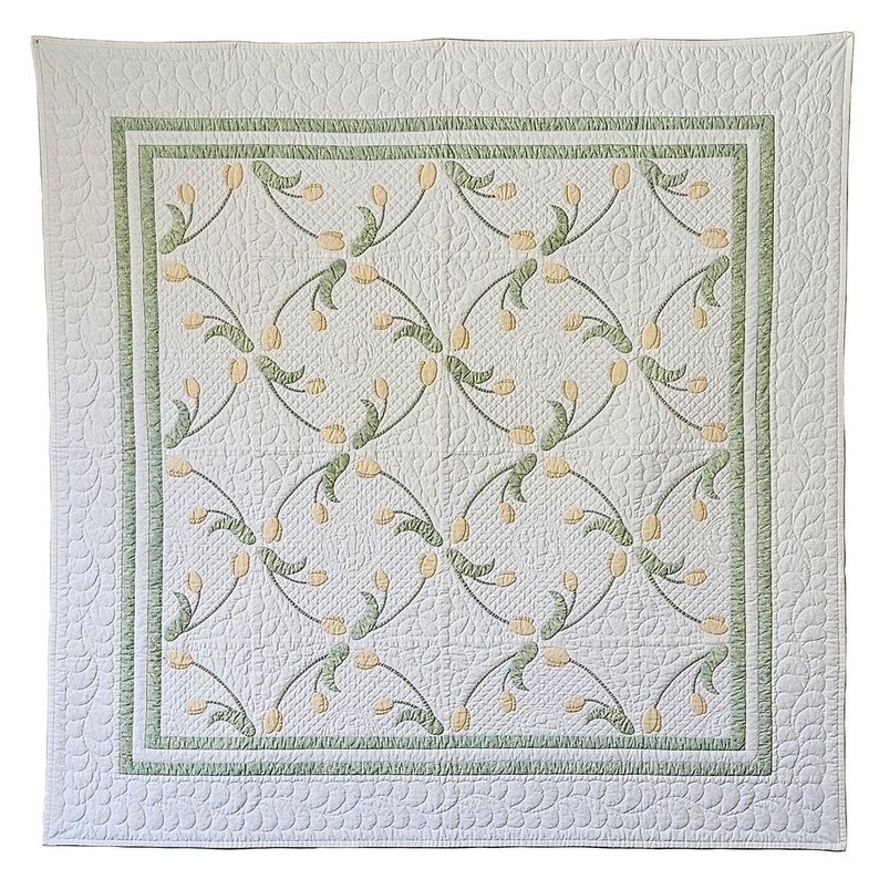 May include: A white quilt with a repeating pattern of yellow tulip-like flowers and green stems. The quilt has a green border and a scalloped edge. The quilting creates a textured effect on the white fabric.