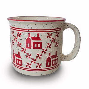 May include: Cream-colored ceramic mug with a red rim and handle, speckled with black dots. The mug features a repeating pattern of red houses and geometric shapes. A charming addition to any kitchen.