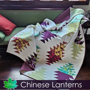 May include: A quilt featuring a white background with repeating tree-like shapes in shades of purple, yellow, and green. The quilt has a dark purple border and visible stitching throughout. The text "Robinson Pattern Company" and "Chinese Lanterns" appears at the bottom.