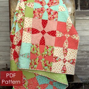 Peut inclure: Une courtepointe colorée avec un motif floral rouge, rose, vert et bleu. La courtepointe est pliée sur un objet métallique. Le texte "PDF Pattern" et "Cotton Fields" sont visibles.