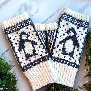 May include: A pair of ivory and navy blue knitted fingerless gloves. The gloves feature a repeating pattern of a penguin silhouette. The cuffs and fingerless openings are ivory, while the penguin design is navy blue.