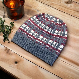 May include: A gray knitted beanie with a red and white geometric pattern. The beanie is made of a soft, warm material and is perfect for cold weather.