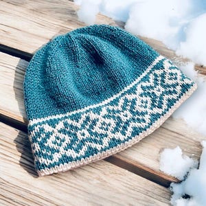 Può includere: Un cappello di lana blu turchese con un motivo geometrico bianco e turchese attorno al bordo.