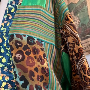 May include: A patchwork garment featuring a variety of patterns and textures. The design incorporates leopard print, striped fabric, and a batik-style pattern in shades of blue, green, brown, and yellow. The garment has a loose, flowing silhouette.