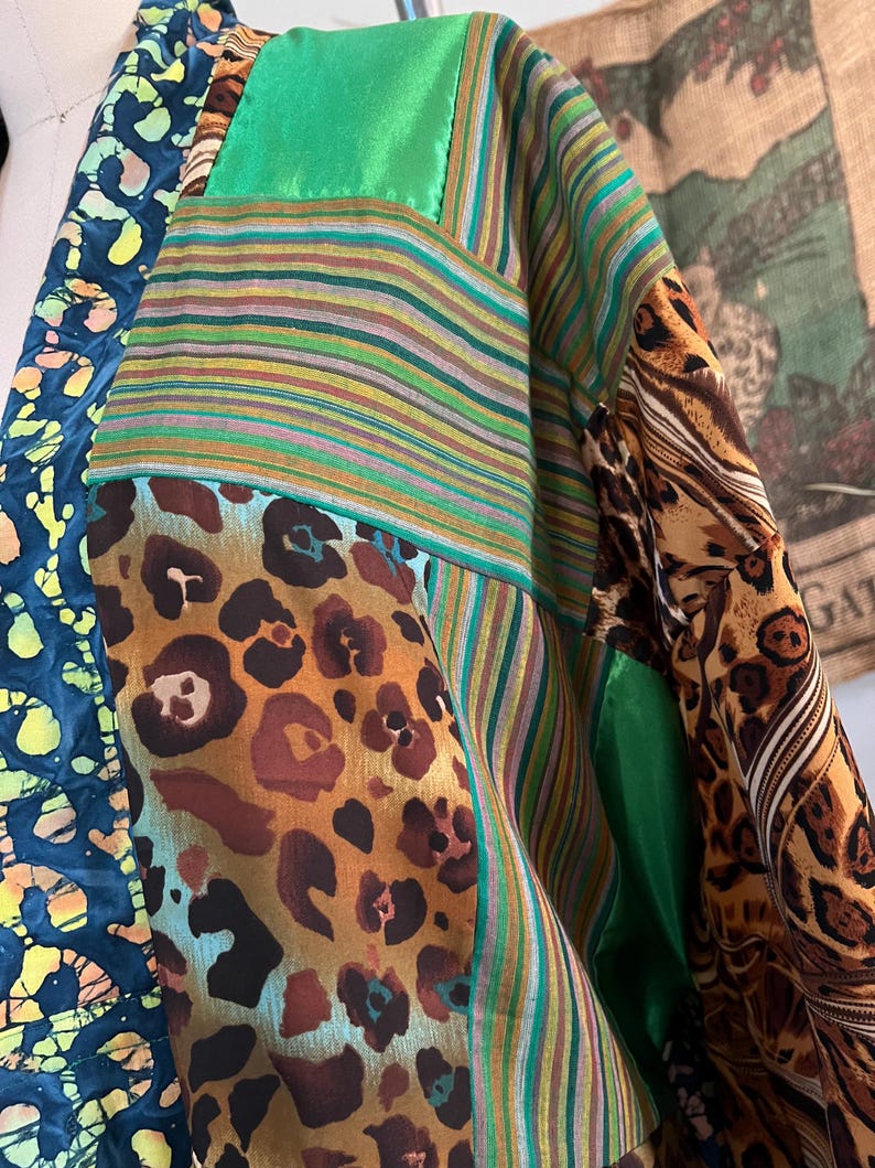 May include: A patchwork garment featuring a variety of patterns and textures. The design incorporates leopard print, striped fabric, and a batik-style pattern in shades of blue, green, brown, and yellow. The garment has a loose, flowing silhouette.