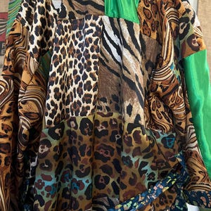 May include: A patchwork robe featuring a variety of animal prints, including leopard, zebra, and tiger stripes. The robe has green satin accents and a patterned belt. The garment is made of a silky material.
