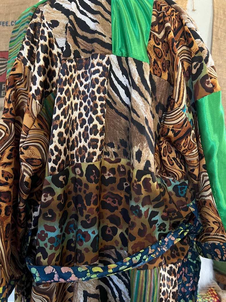 May include: A patchwork robe featuring a variety of animal prints, including leopard, zebra, and tiger stripes. The robe has green satin accents and a patterned belt. The garment is made of a silky material.