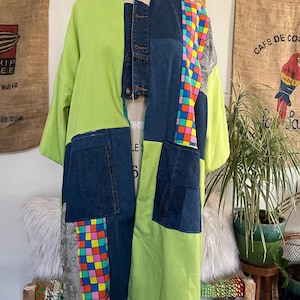 May include: A patchwork jacket featuring lime green fabric panels, dark blue denim sections with visible pockets, and colorful checkered patterns. The garment includes a central denim placket with buttons and black and white geometric print accents.