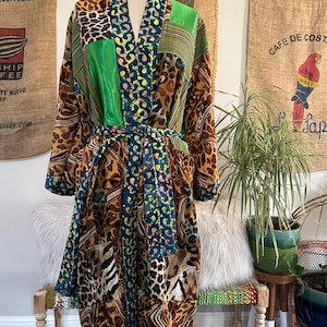 May include: A patchwork robe with a mix of animal prints, green, and blue patterns. The robe is displayed on a mannequin and has a matching belt. The robe's design includes leopard and zebra prints, and striped and polka dot patterns.