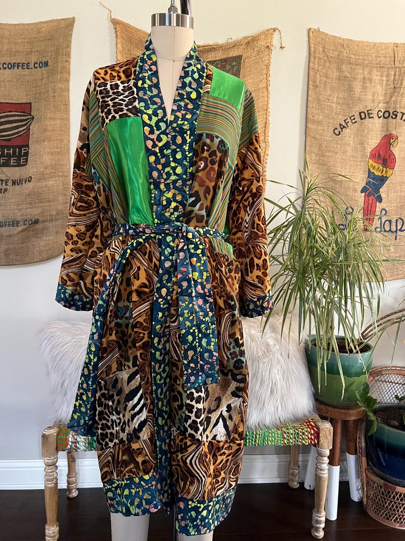 May include: A patchwork robe with a mix of animal prints, green, and blue patterns. The robe is displayed on a mannequin and has a matching belt. The robe's design includes leopard and zebra prints, and striped and polka dot patterns.
