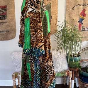 May include: A long, patchwork robe with a vibrant mix of patterns and colors. The robe features leopard print, green satin panels, and floral accents. The robe is displayed on a mannequin, showcasing its flowing design and unique style.