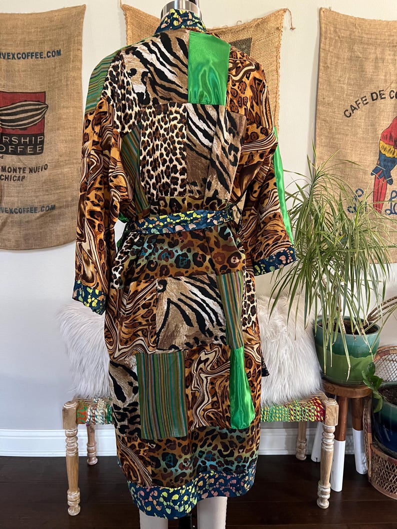 May include: A long, patchwork robe featuring a mix of animal prints, including leopard and zebra patterns, with green and striped accents. The robe has a matching belt and is displayed on a mannequin. The robe's hemline and cuffs have a dark blue and yellow floral design.