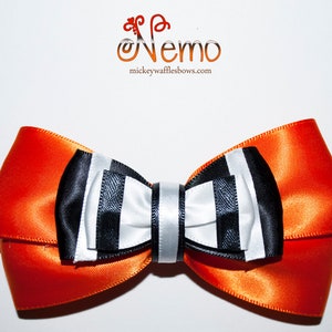 Peut inclure: Un grand nœud orange avec un centre rayé blanc et noir. Le nœud est fait de ruban de satin et a un design simple et élégant.