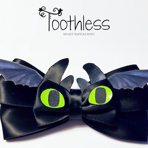 Puede incluir: Lazo de satén negro con ojos verdes y alas negras, que se asemeja a Chimuelo de Cómo entrenar a tu dragón. El lazo está decorado con el texto "Toothless" y "Mickey Waffles Bows".