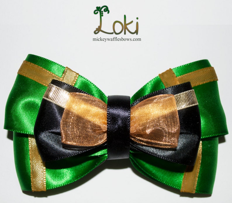 May include: A green, black, and gold bow with a black center. The bow is made of satin and tulle.