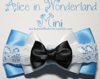 以下が含まれることがあります： レースのトリムが付いた青、白、黒のリボン。リボンには「Alice in Wonderland Mini」というテキストと「mickeywafflesbows.tumblr.com」というウェブサイトが飾られています。