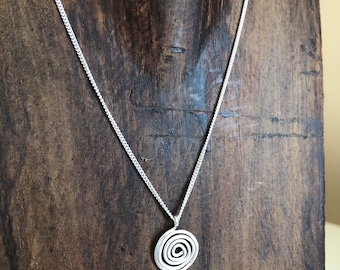 May include: A silver chain necklace with a spiral pendant. The pendant is a circle with a spiral design in the center.