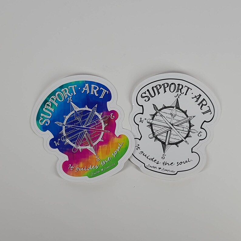 May include: Two die-cut stickers with a compass design. One features a colorful tie-dye background with the words "SUPPORT ART" and "It guides the soul." The other is black and white with the same text.