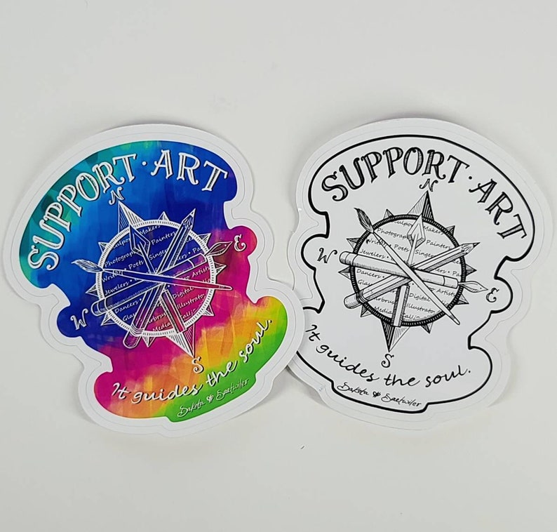 May include: Two die-cut stickers with a compass design. One features a watercolor rainbow background, the other is black and white. Both say "SUPPORT ART" and "It guides the soul."