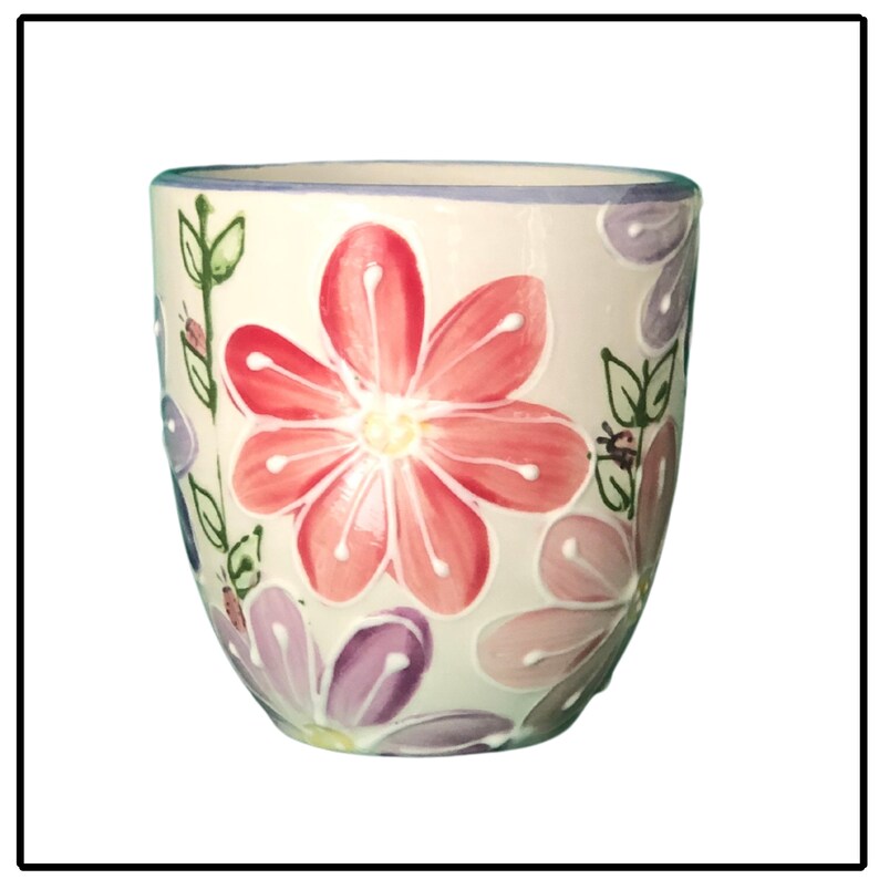 May include: A white ceramic mug with a floral design. The mug features pink, purple, and green flowers with a white background.