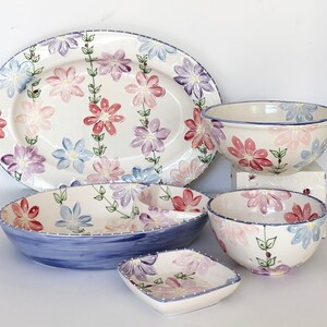May include: A set of five ceramic dishes featuring a floral design in shades of pink, purple, and blue. The set includes a large oval platter, two bowls, and two smaller dishes.