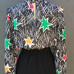 Puede incluir: Mono negro y blanco con una parte superior de manga larga transparente con un estampado de estrellas de colores. La parte superior tiene un cuello alto y una espalda con abertura.
