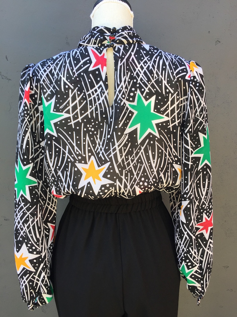 Puede incluir: Mono negro y blanco con una parte superior de manga larga transparente con un estampado de estrellas de colores. La parte superior tiene un cuello alto y una espalda con abertura.
