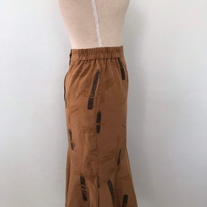 May include: A brown midi skirt with a black abstract pattern. The skirt has an elastic waistband and a flared hem.