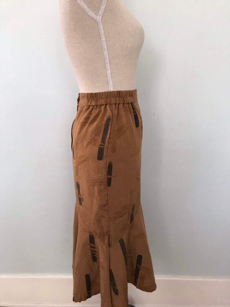 May include: A brown midi skirt with a black abstract pattern. The skirt has an elastic waistband and a flared hem.