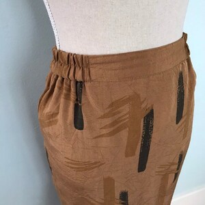 May include: A brown skirt with a black and brown abstract print. The skirt has an elastic waistband and a zipper closure.