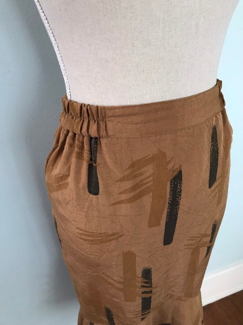 May include: A brown skirt with a black and brown abstract print. The skirt has an elastic waistband and a zipper closure.
