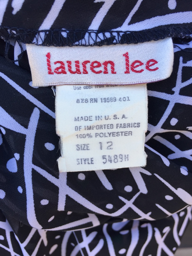 Puede incluir: Una etiqueta blanca con texto negro sobre una tela estampada en blanco y negro. La etiqueta dice "lauren lee", "828 RN 19569-401", "MADE IN U.S.A.", "OF IMPORTED FABRICS", "100% POLYESTER", "SIZE 12" y "STYLE 5489H".