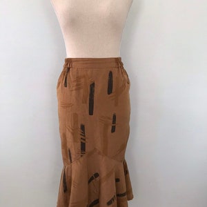 May include: A brown midi skirt with a black abstract print. The skirt has a ruffled hem and an elastic waistband.