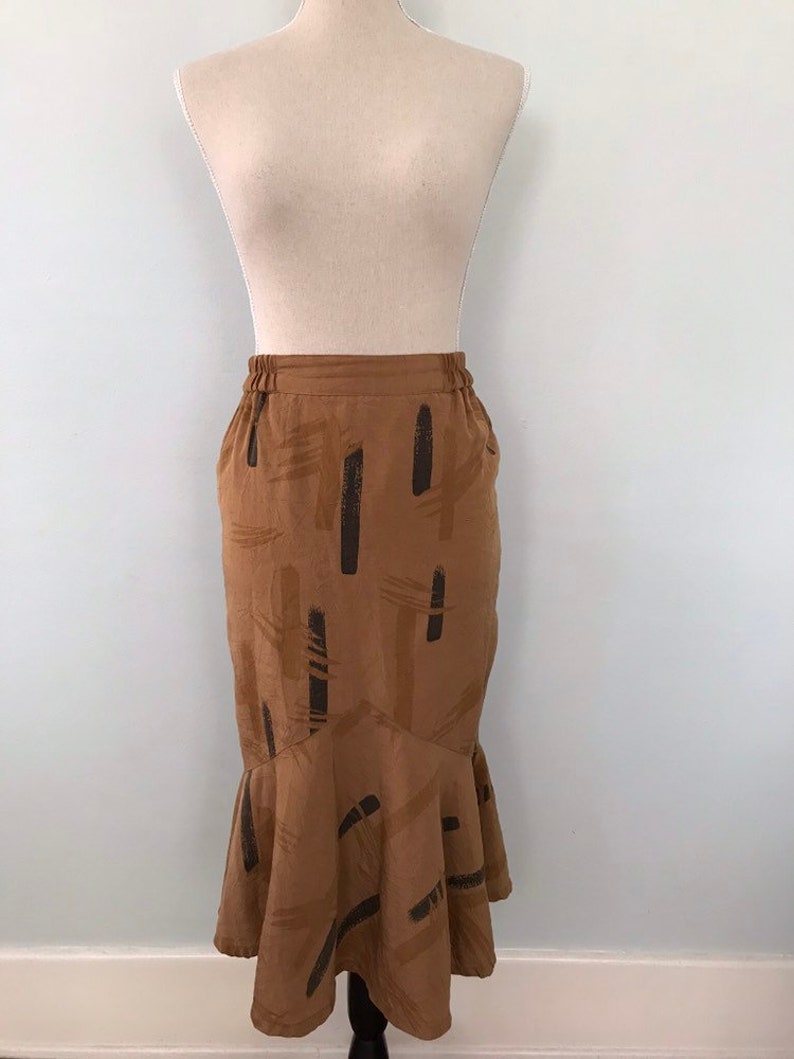 May include: A brown midi skirt with a black abstract print. The skirt has a ruffled hem and an elastic waistband.