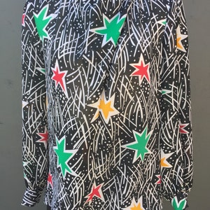 Puede incluir: Una blusa negra de manga larga con un estampado de estrellas de colores. Las estrellas son rojas, verdes, amarillas y blancas. El fondo es negro con l&iacute;neas blancas.