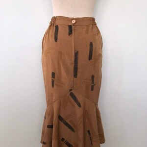 May include: A brown midi skirt with a black abstract print. The skirt has a fitted waist and a flared hem.