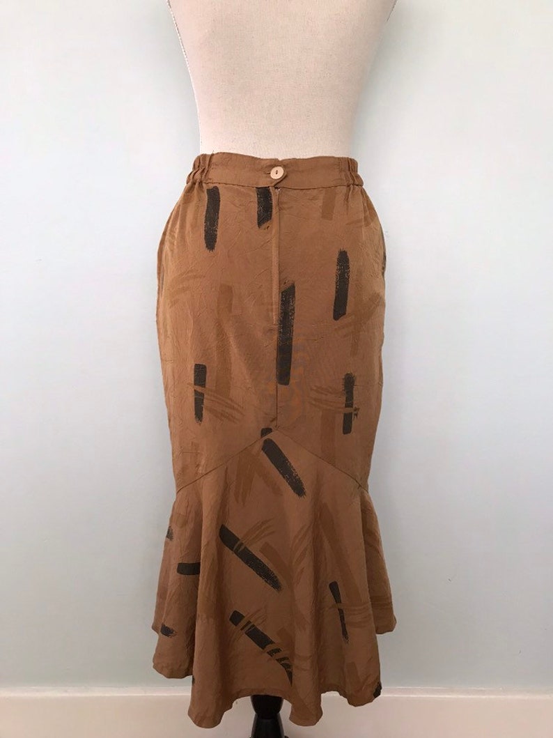 May include: A brown midi skirt with a black abstract print. The skirt has a fitted waist and a flared hem.