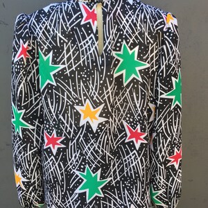 Puede incluir: Una blusa negra de cuello alto y mangas largas. La blusa tiene un estampado de estrellas blancas, verdes, rojas y amarillas sobre un fondo negro.
