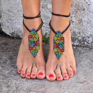 May include: A pair of colorful beaded foot jewelry with black cords. The jewelry features a geometric pattern of hexagons in shades of red, orange, yellow, green, blue, and purple.