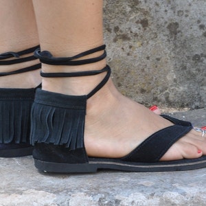 May include: Black leather sandals with fringe detailing and ankle ties. The sandals have a flat sole and are made of a soft, supple leather.